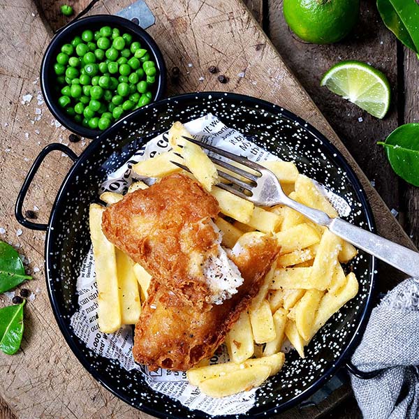 Fish 'n chips anrettet på tallerken med lime og grønne erter ved siden av.
