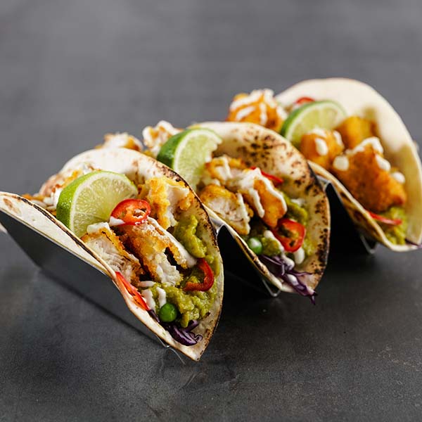 Stativ med små tortilla fylt med fisketaco; fiskepinner, guacamole, erter, rødkål, chili, limebåt