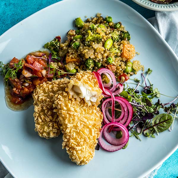 Røstipanert fisk anrettet på tallerken med quinoapilaff, salsa, salat og syltet rødløk.