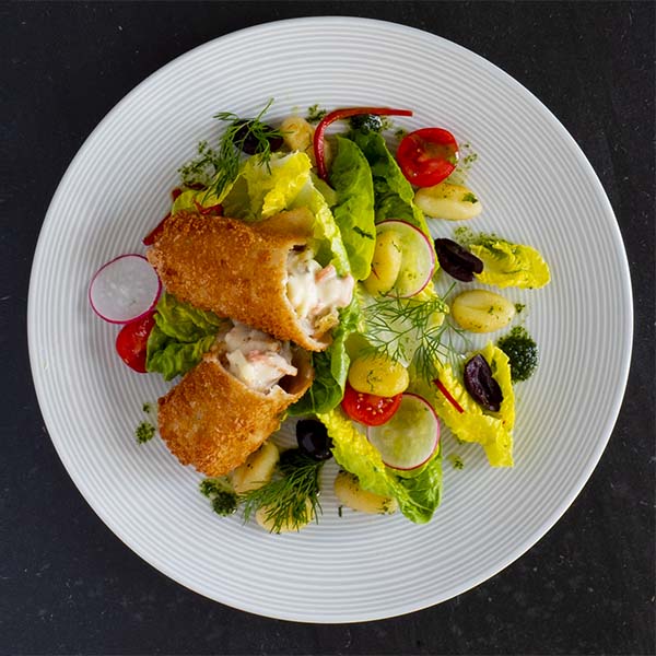 Sprøbakt fiskerullade anrettet på tallerken med gnocchi, hjertesalat, reddik og cherrytomat.